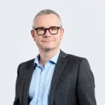 Personne portant un costume sombre et une chemise claire sur fond neutre