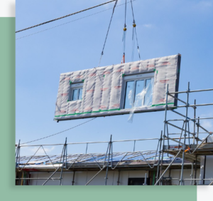 Grue soulevant un module préfabriqué avec fenêtre sur un chantier équipé d’un échafaudage