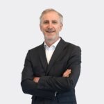 Personne portant un costume sombre avec les bras croisés sur fond clair