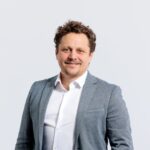 Personne portant une veste gris clair et une chemise blanche sur fond clair